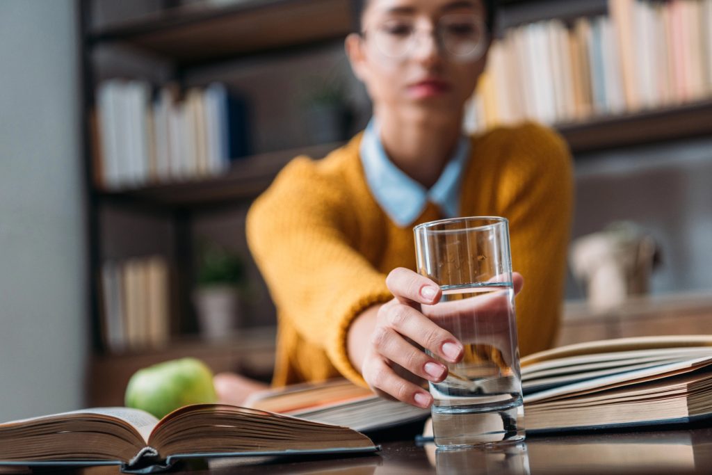 A woman setting a glass of water on a table in front of multiple books