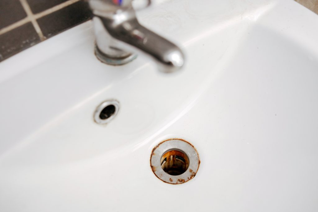 A metal tub drain hole with red rust iron stains.