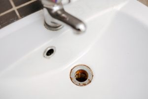 A metal tub drain hole with red rust iron stains.