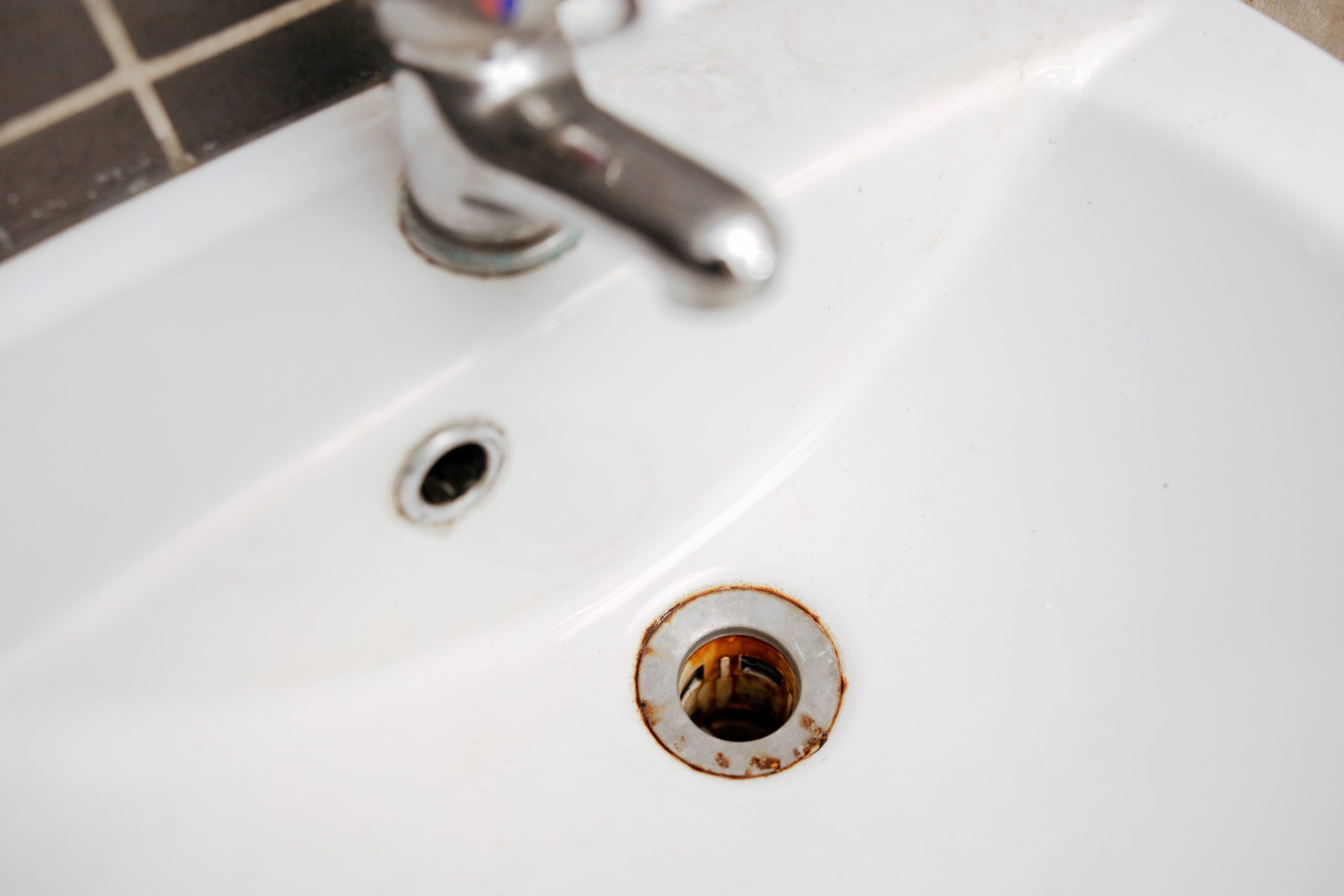 A metal tub drain hole with red rust iron stains.