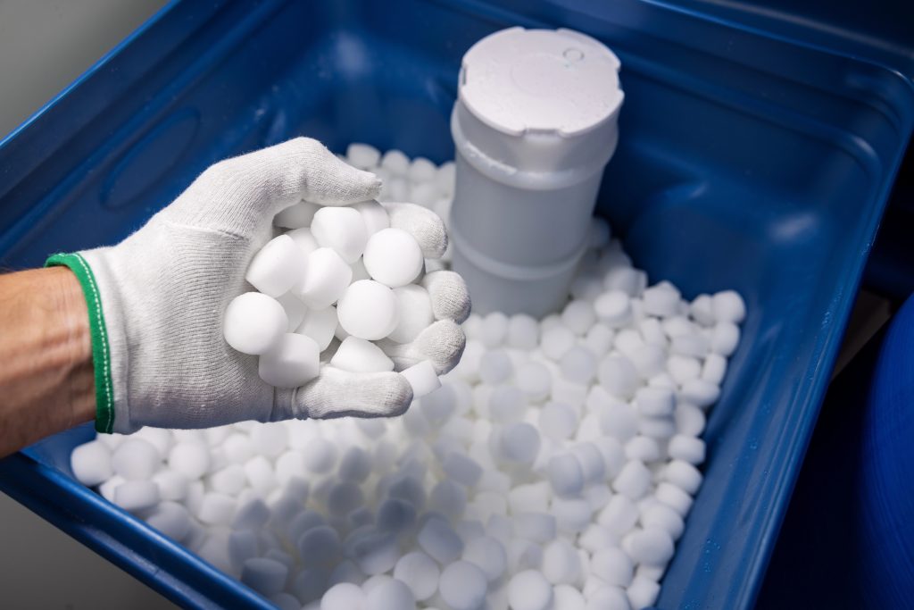 A white-gloved hand holding a fistful of water softeners over a bucket of water softeners.